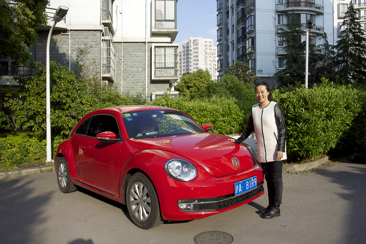 Photo de la série la Chine Rouge? femme chinoise dans la banlieu de shanghai qui montre fièrement sa voiture volkswagen rouge